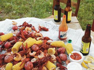 A Low Country boil, served on a picnic table covered in newspaper with cocktail sauce, lemon wedges, hot sauce, and beer.