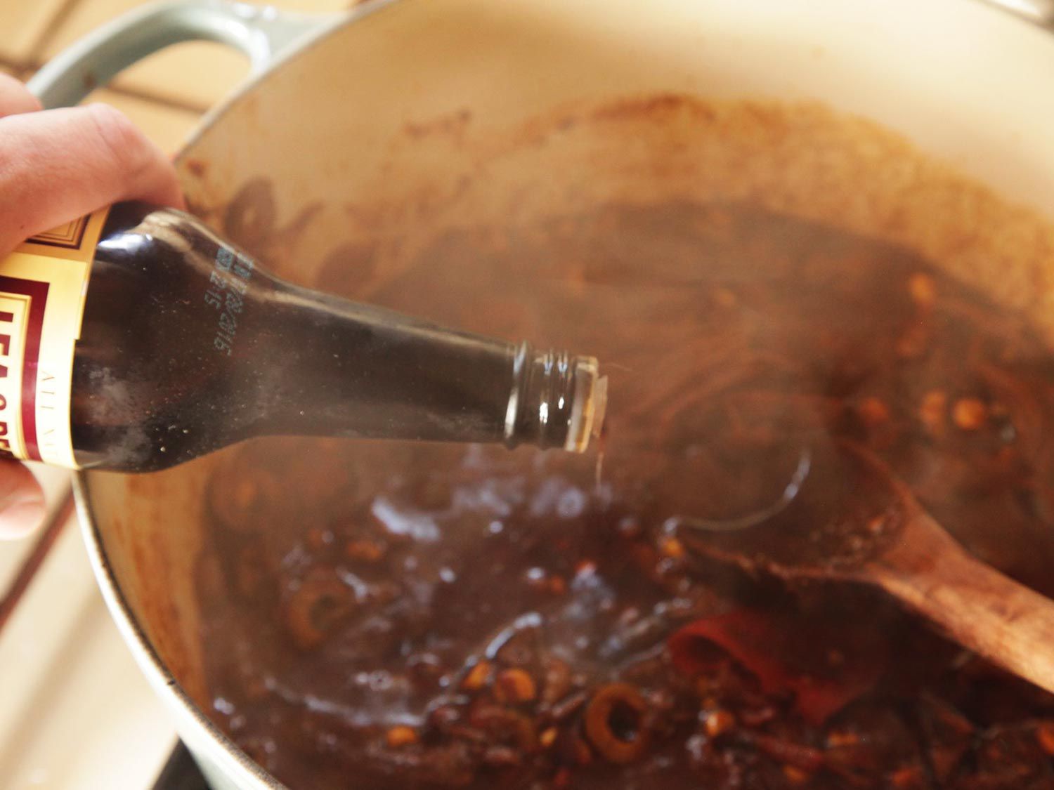 Pouring Worcestershire sauce into a pot of braising meat