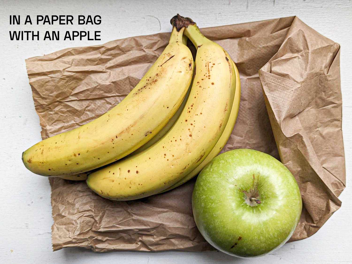 A bunch of bananas that were stored in a paper bag with an apple; apple shown. They are yellow with a faint tinge of green, and very light brown spotting in some areas.