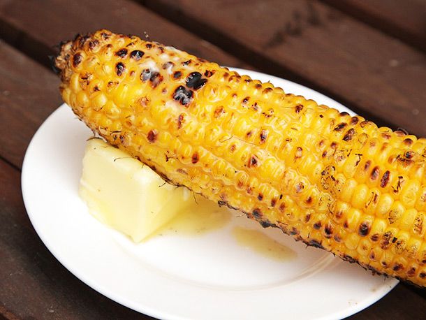 Nicely charred grilled corn on the cob sitting on a melting pat of butter.