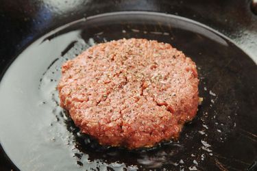 A seasoned burger patty made of Beyond Burger, frying in a cast iron skillet.
