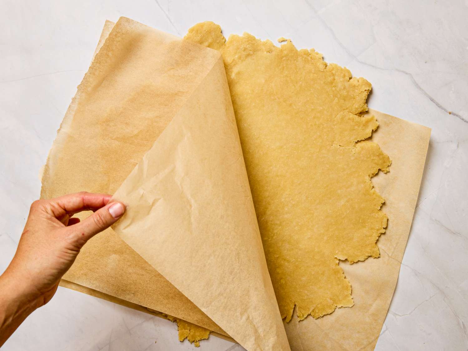 Person peeling parchment paper from a rolledout piece of pie dough
