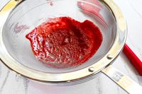 All-Clad Stainless-Steel Strainer, Set of 3 with red puree being pressed through accompanied by a kitchen utensil handle visible in the background