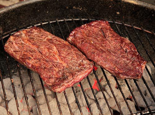 A halved ribeye cap is grilled over hot coals.