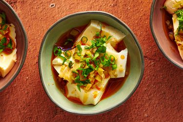An irregularly round glazed ceramic bowl holding silken tofu with soy sauce and chili oil. There are two additional bowls, one on the right periphery of the image, one on the left periphery.
