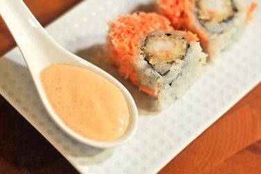 An Asian spoon holding spicy mayonnaise on a platter of sushi. 