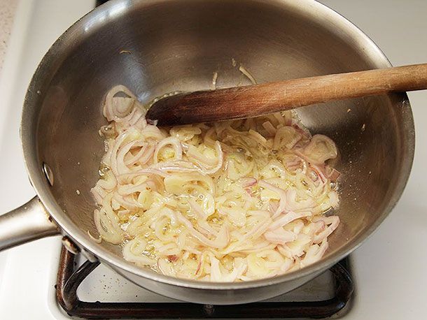 Sliced shallots and garlic are cooked in a large saucier pan.