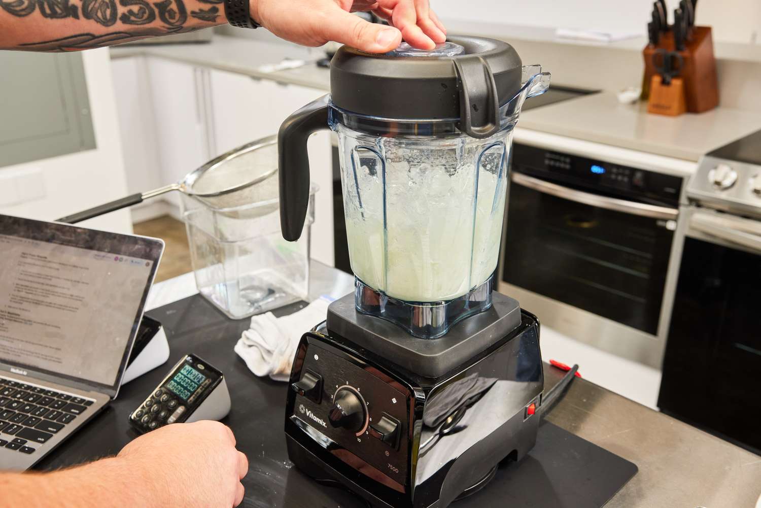 Hand resting on top of a Vitamix 7500 Blender blending ice and juice
