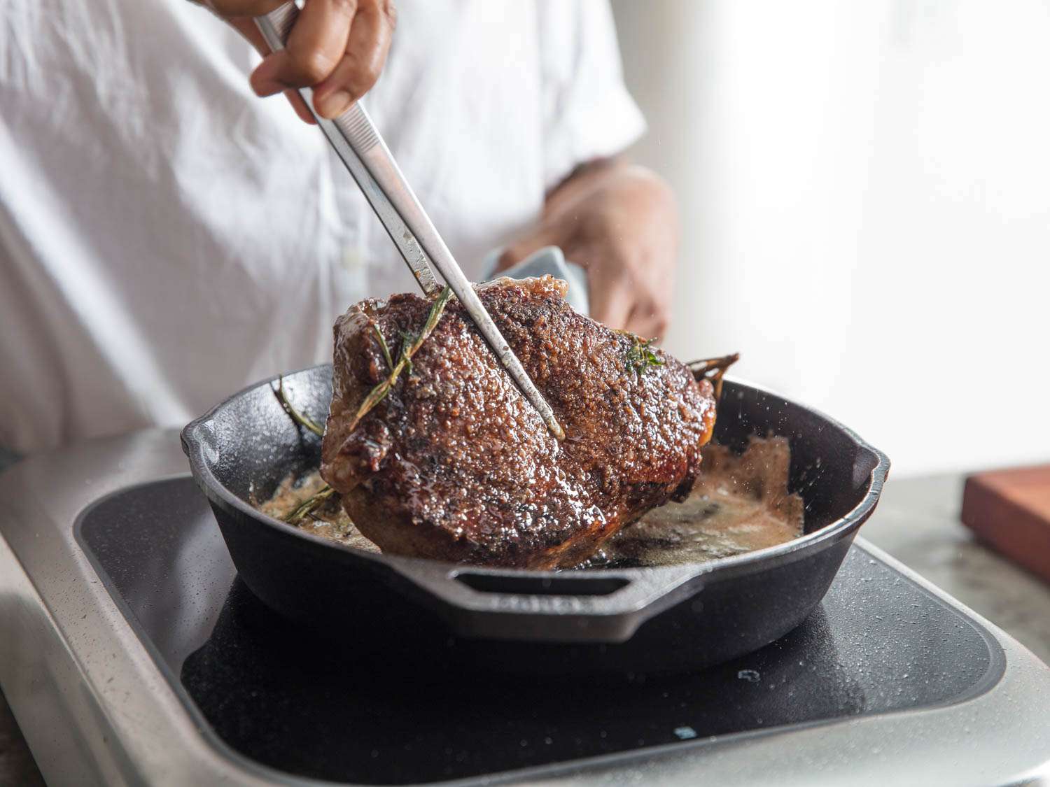 tweezers grabbing a steak out of a cast iron pan