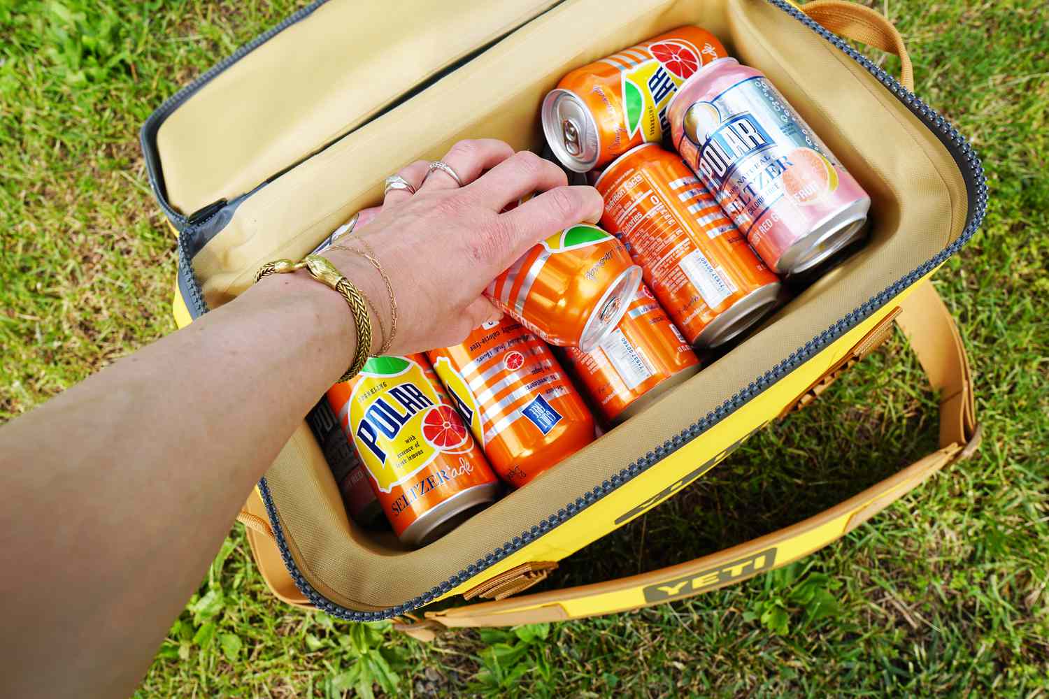 A person adding a can of seltzer to a soft cooler