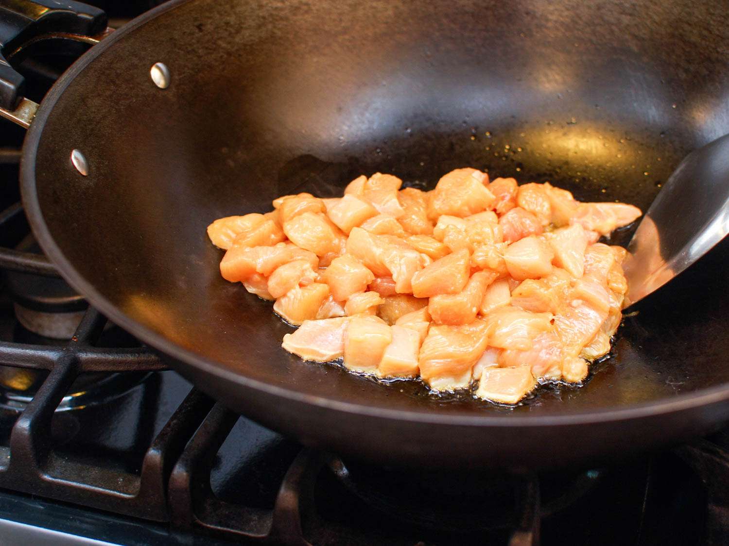 Cooking diced chicken in a wok for cashew chicken ding.
