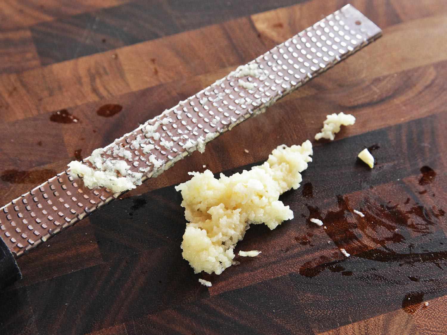 Close-up of garlic being grated with a microplane onto a cutting board.