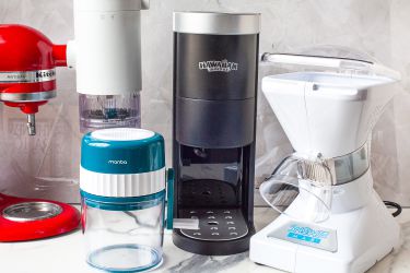 Kitchen countertop with various ice shaving appliances and a red KitchenAid mixer