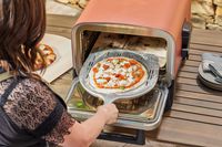 A person placing a pizza into the Ninja Woodfire 8-in-1 Outdoor Oven