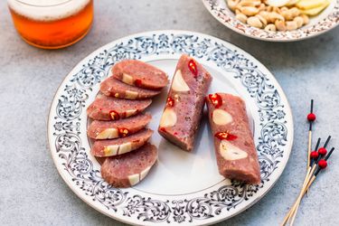 A plate of sliced nem chua, flanked by toothpicks for serving and a glass of beer.