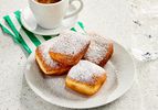 Beignets on a white plate with powdered sugar, with a coffee, green and white striped napkin, and a marble surface