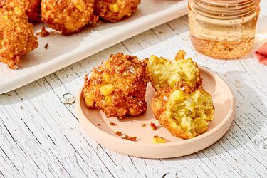 Plate of southern corn fritters nearby a tray of fritters and a glass of beverage