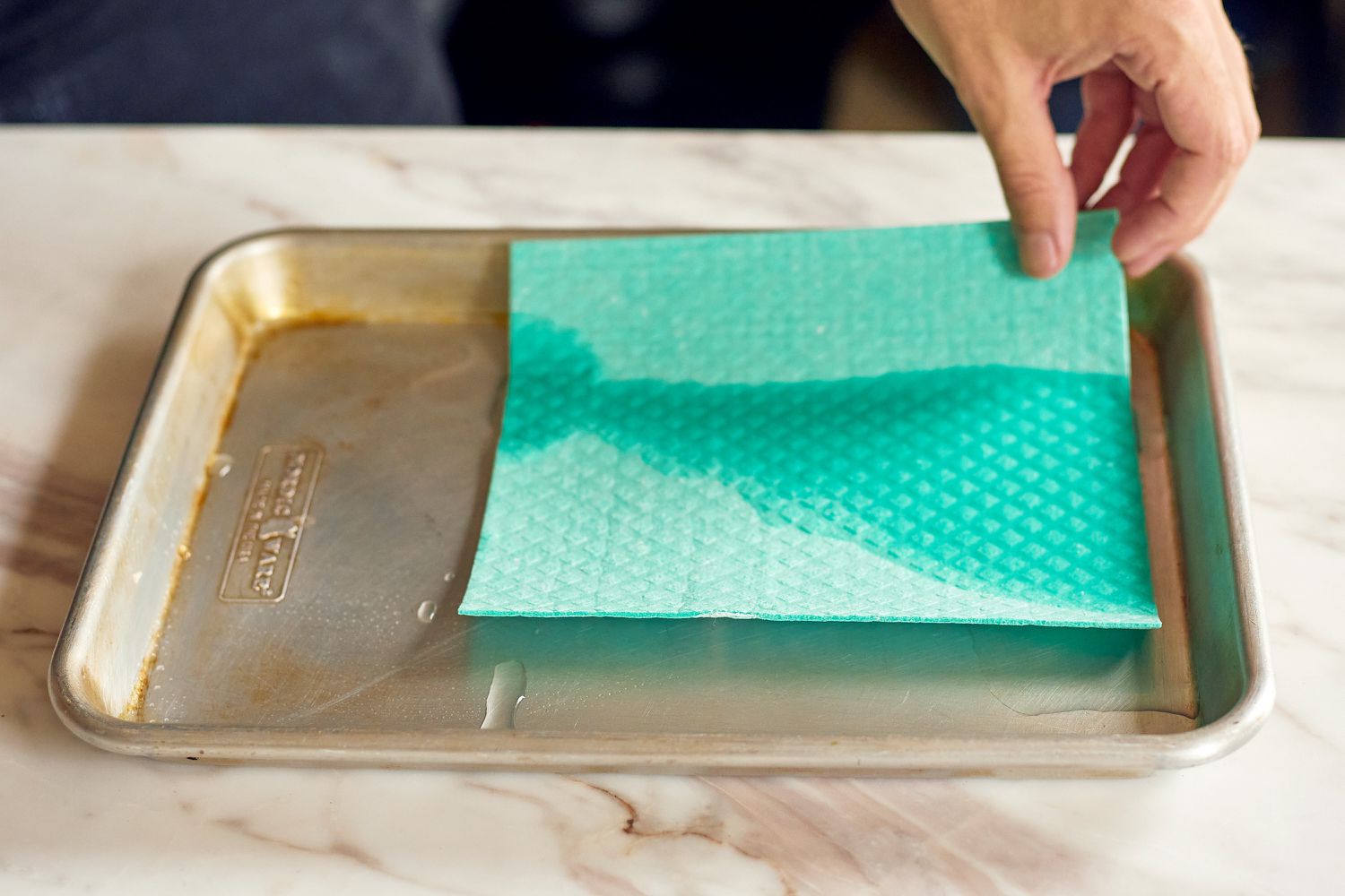 A person dipping a blue Swedish dishcloth in a pan of water.