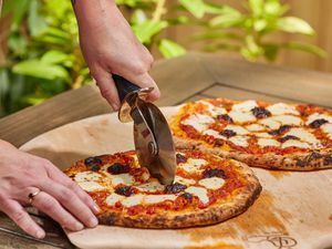 A person cutting a pie made in the Solo Stove Pi Prime Pizza Oven