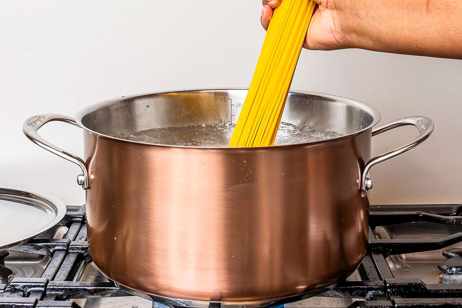A hand placing pasta into a pot from the Cuisinart Copper Collection Tri-Ply Cookware 8-Piece Set