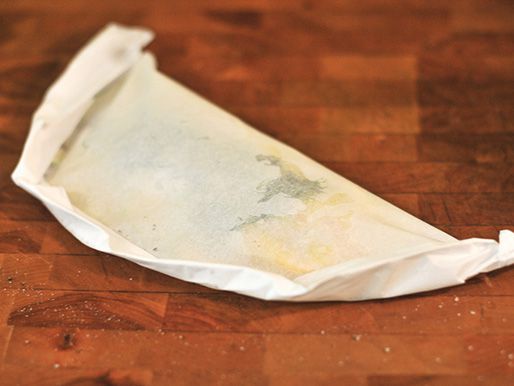 A parchment pouch folded, containing fish and squash, ready for the grill.