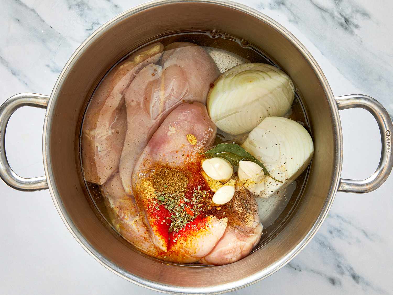 Pot containing raw chicken onion garlic spices and herbs