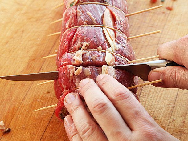 Slicing into a large piece of rolled flank steak that's tied with twine and skewered 