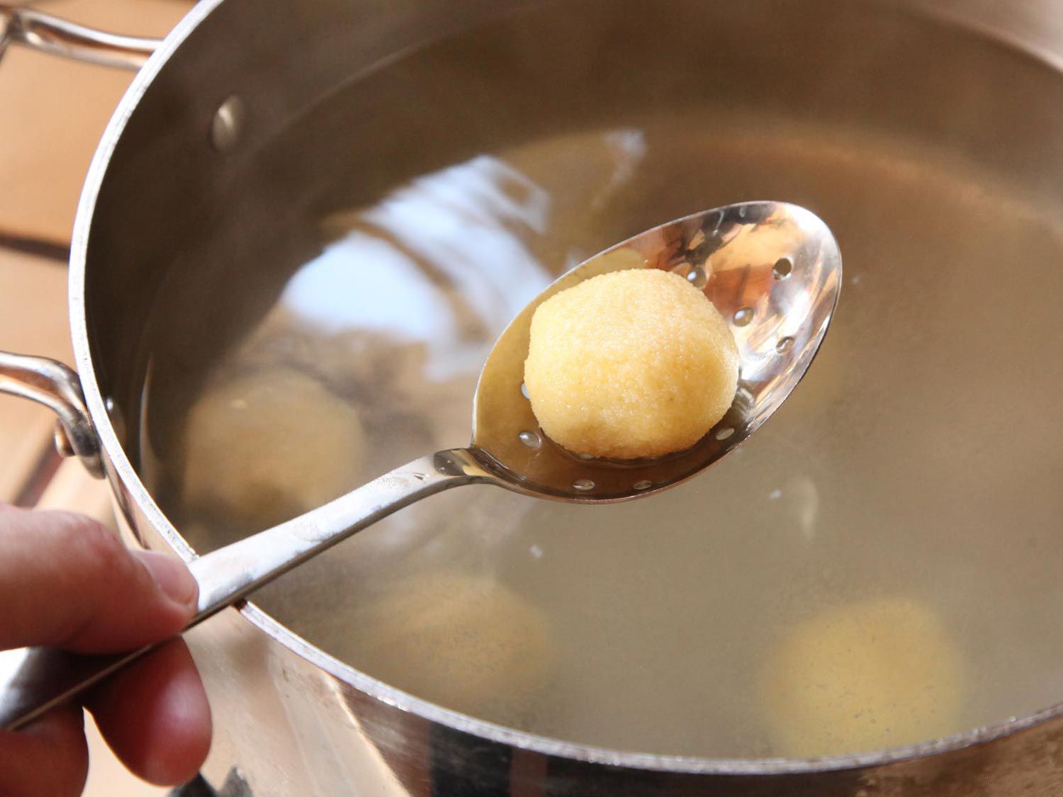 A boiled gnudi in a spoon, overlooking the pot of boiling water containing gnudi. 