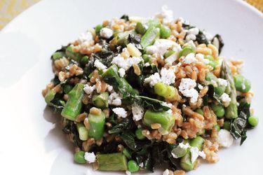 Close-up of warm farro salad with asparagus, peas, and feta, mounded on a white plate.