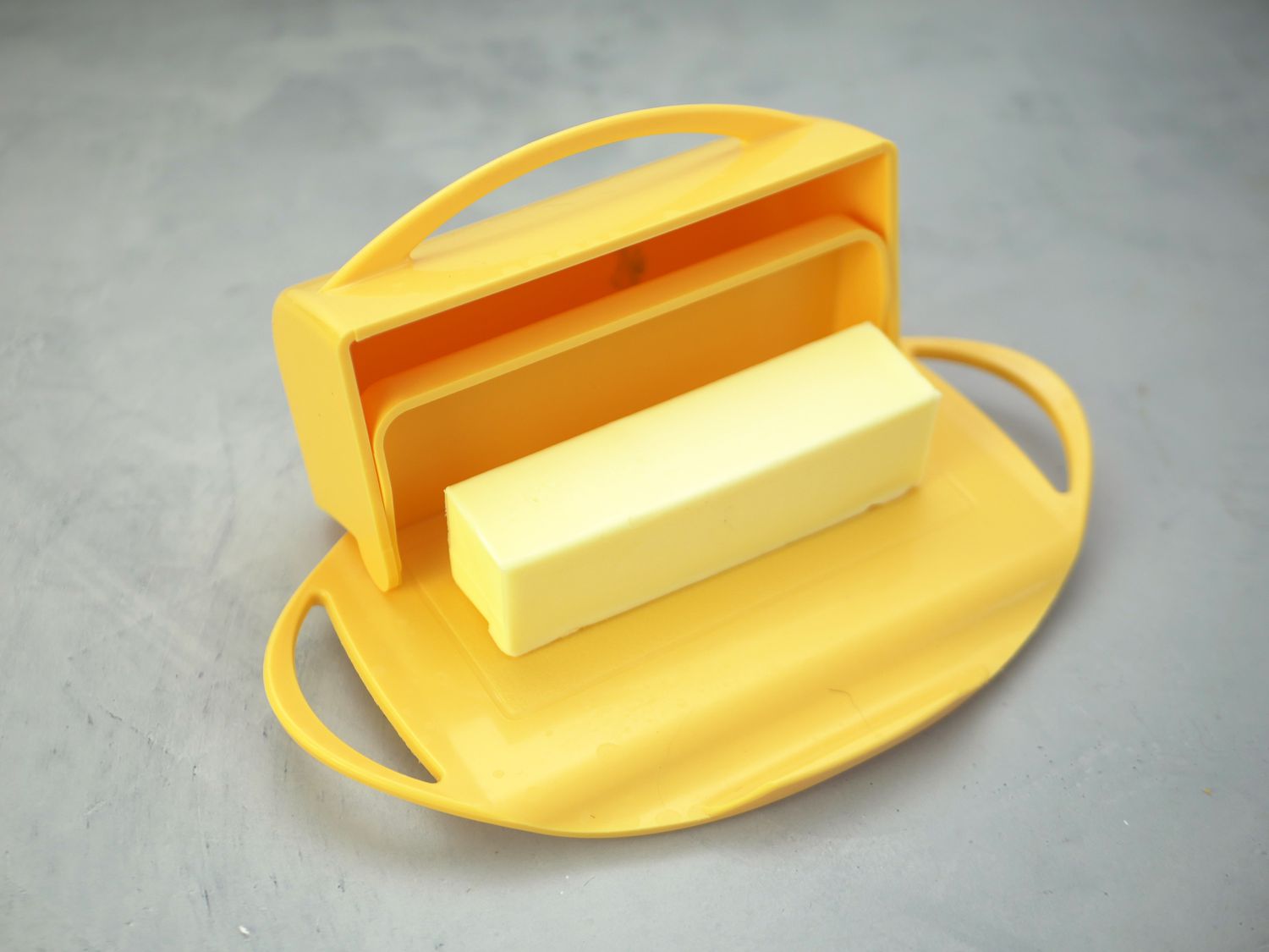 yellow butterie dish with lid opened at hinge and stick of butter inside