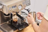A person makes a cappuccino using the Breville BES920XL Dual Boiler Espresso Machine