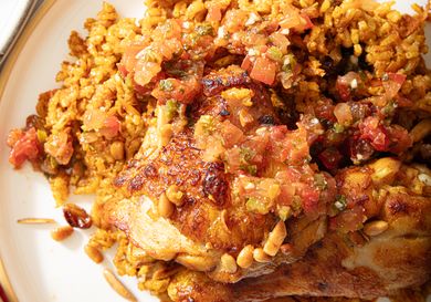 A closeup of a cooked dish with seasoned rice and chicken topped with a diced tomato mixture