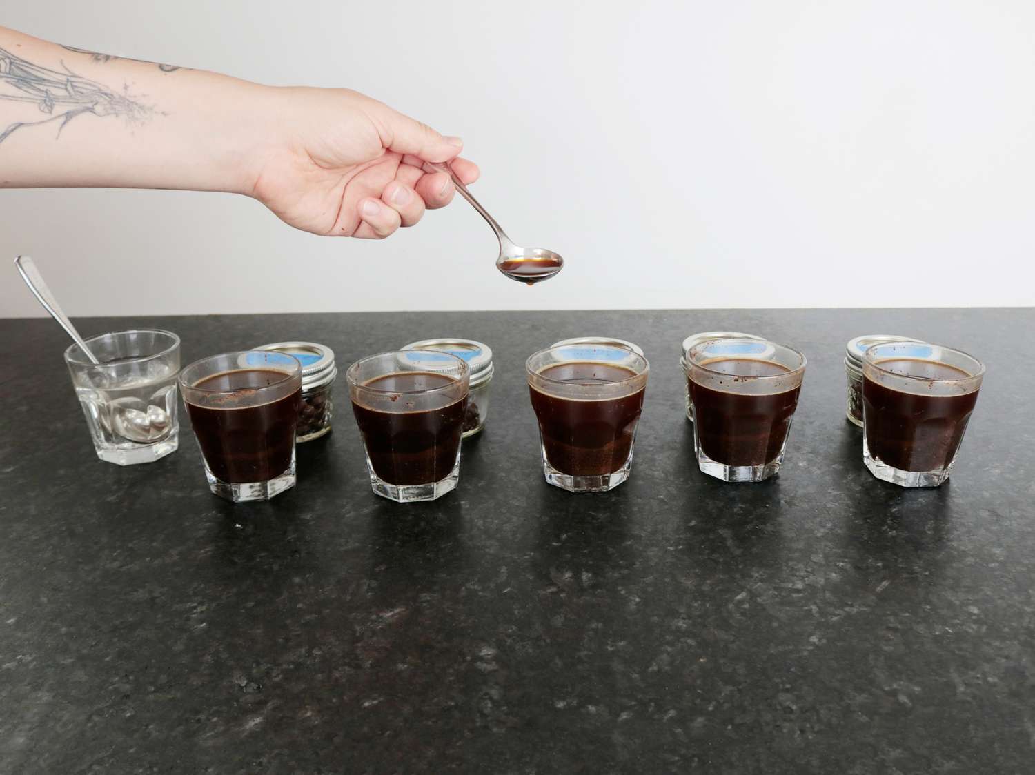 a coffee cupping with brewed coffee in glasses and a spoon taking a small amount of coffee for tasting