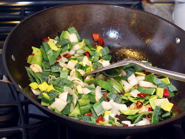 Adding leek greens to a wok containing chiles and garlic. 