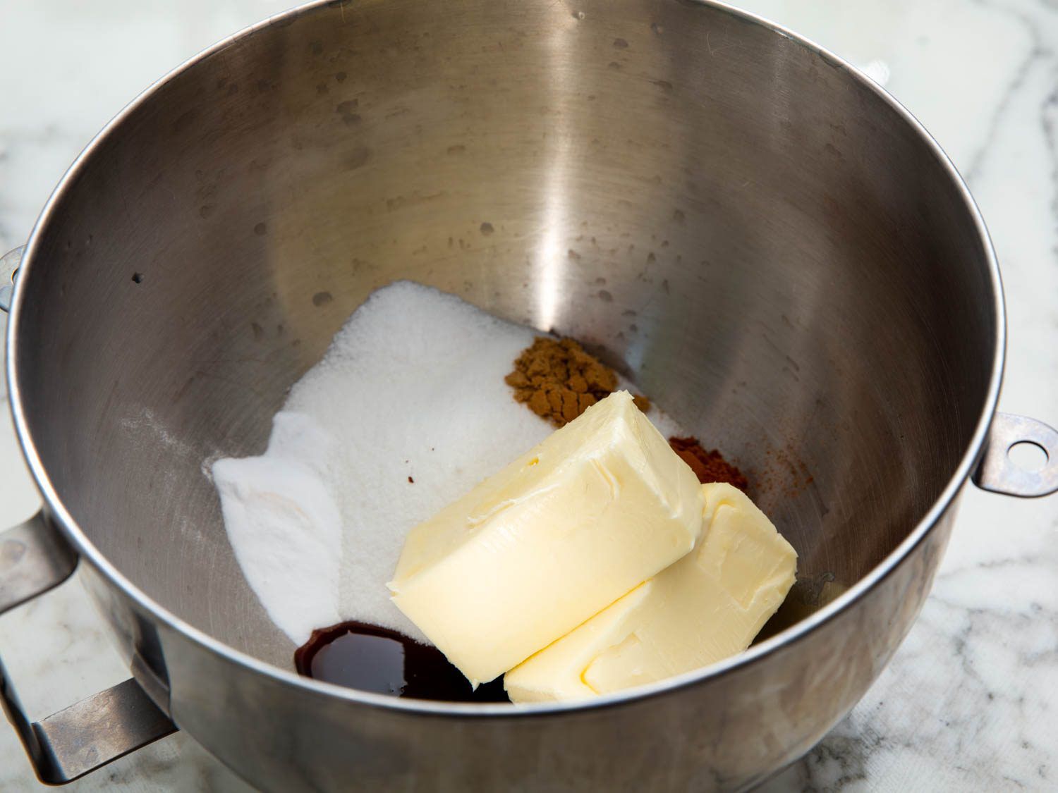 A stand mixer bowl with butter, sugar, barley malt syrup, baking soda, cinnamon, ginger, and salt.