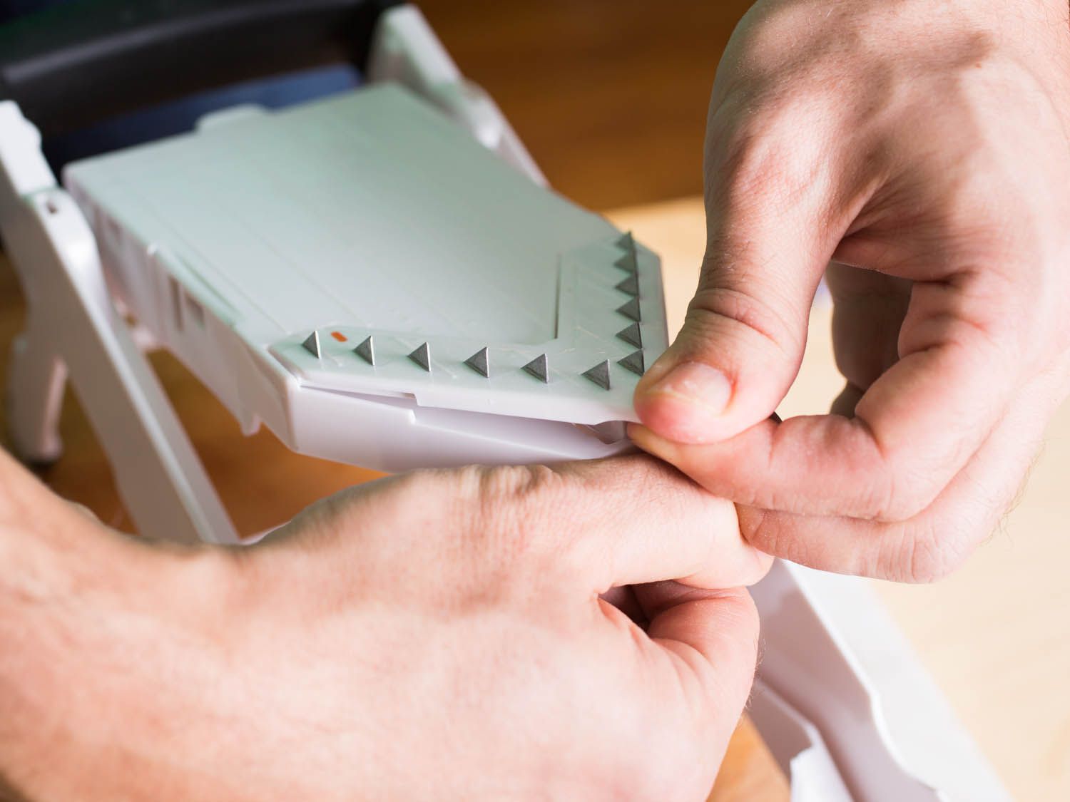Hands removing the OXO Mandoline's serrated teeth attachment