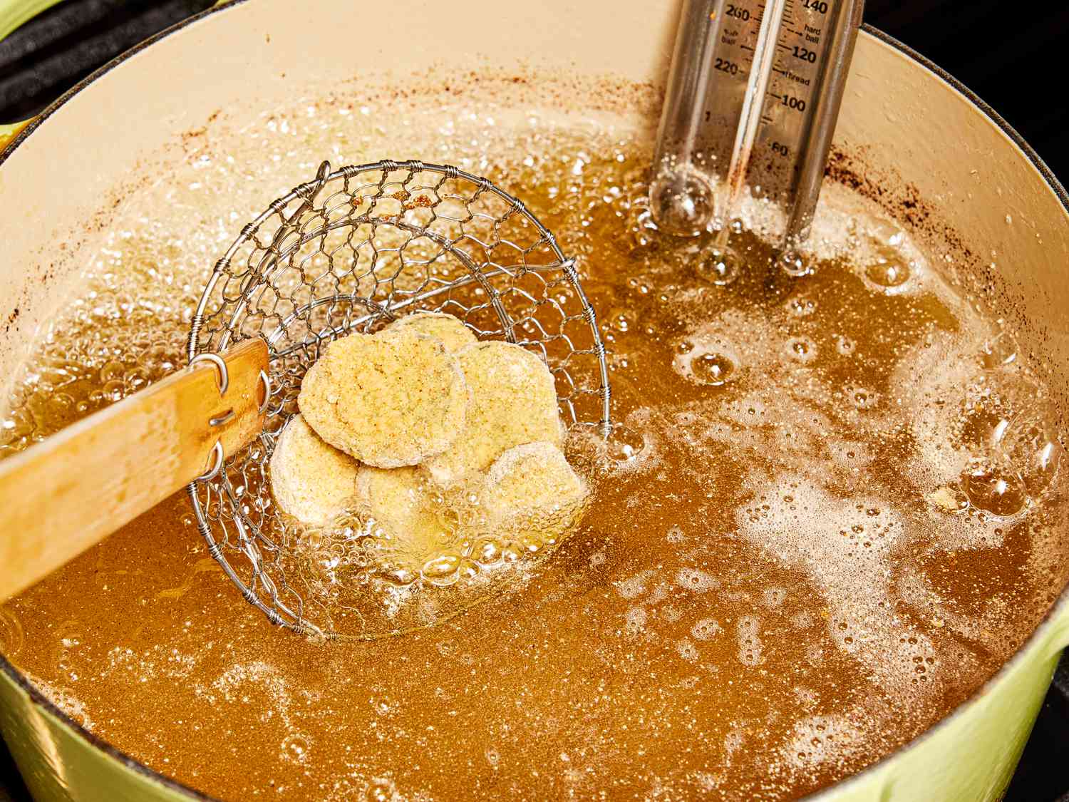 Dipping breaded pickles into heated oil in dutch oven with slotted spoon 