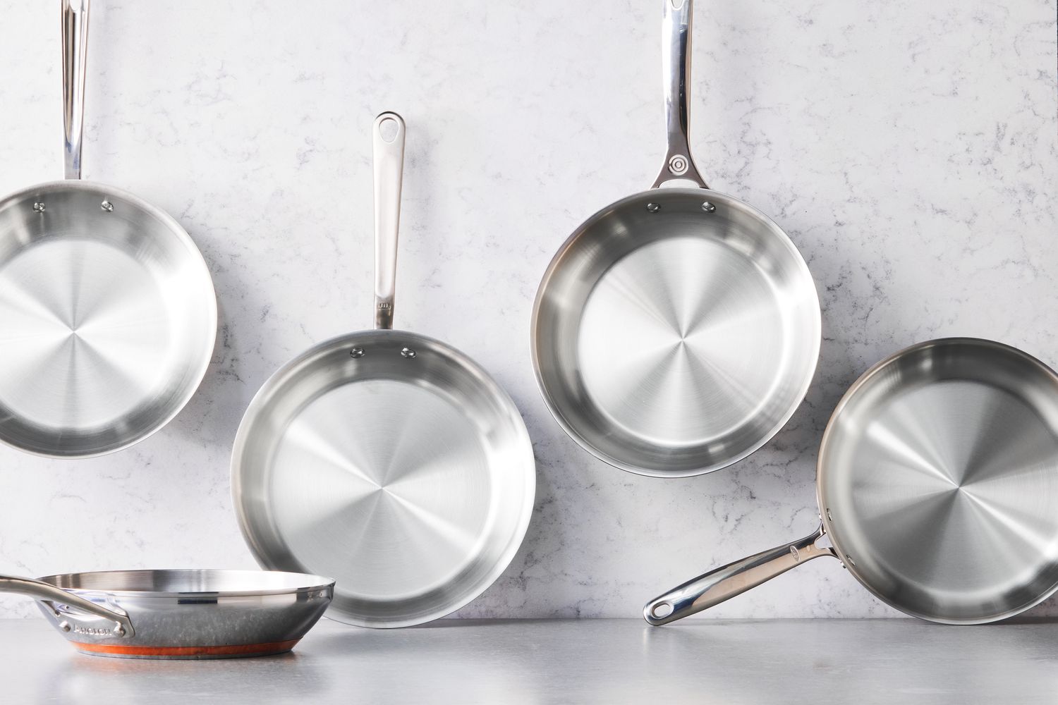 a number of stainless steel skillets against a grey surface