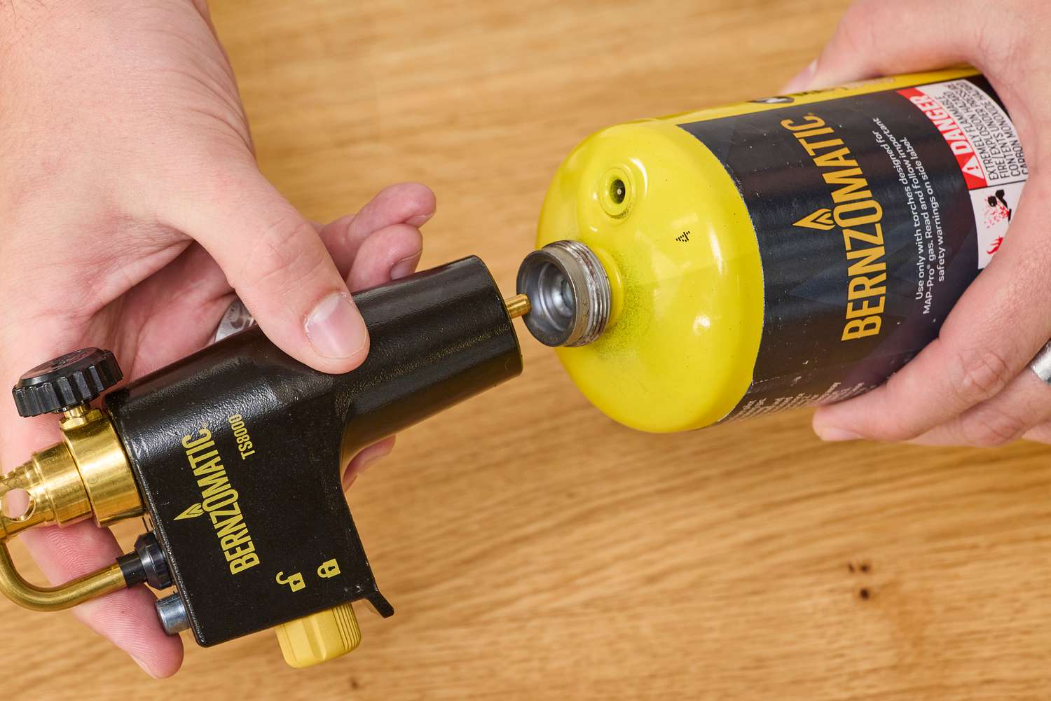 a person attaching the flame part of a torch to a tank of propane