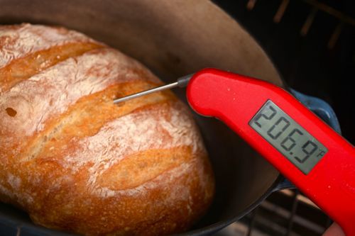 Red instant thermometer poking into crust of golden brown loaf of bread