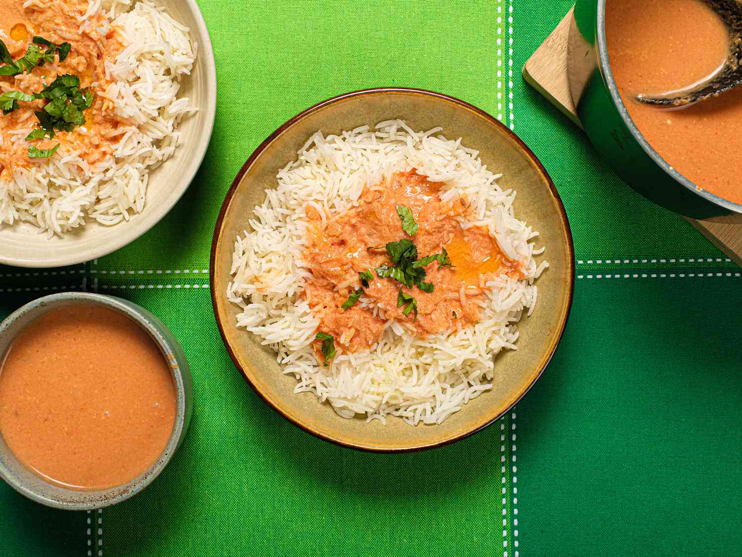 3 bowls of rice and Tomato Coconut soup, dutch oven on the side, and green tabletop.