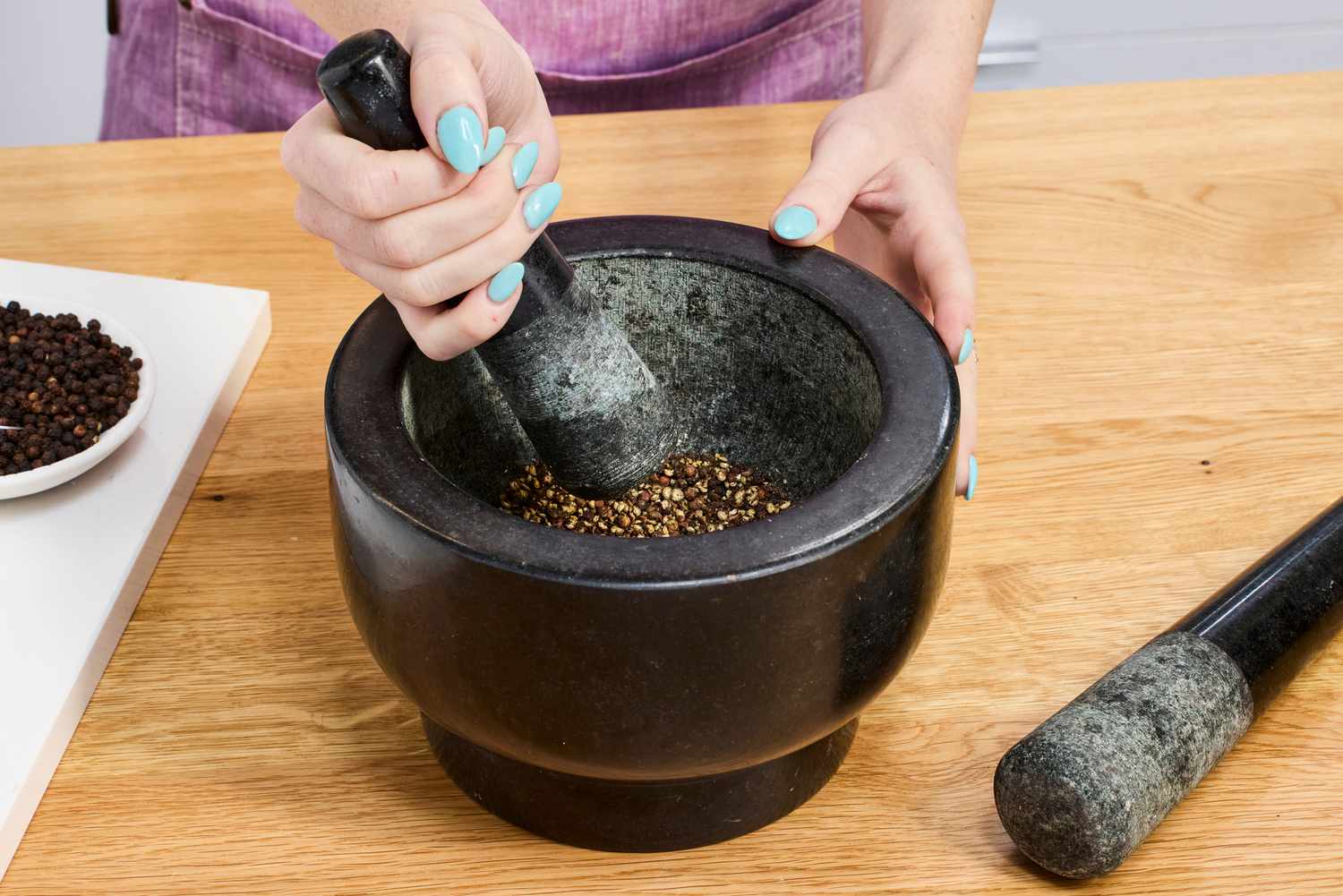 A person using a granite mortar and pestle to crush peppercorns.