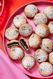 pink platter of fried oreos, two with bite taken out and middle showing. Red background and red basket of oreos on the side, and pink and red napkins. 