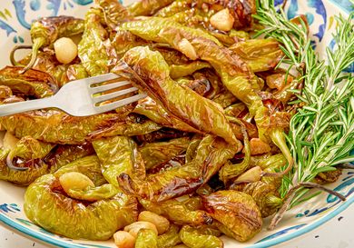A plate of roasted peppers garnished with garlic and rosemary a fork resting on them