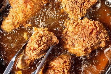 Closeup of fried chicken pieces being cooked in oil with tongs