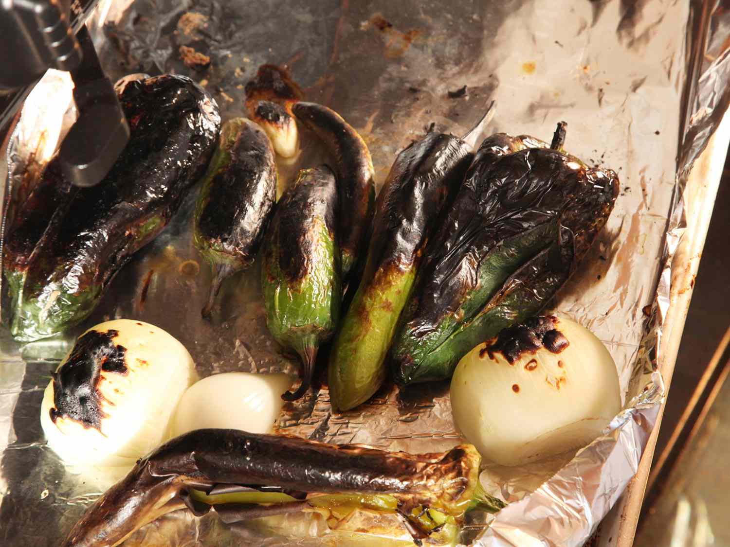 Foil-lined sheet of charred green chiles, garlic, and onion.