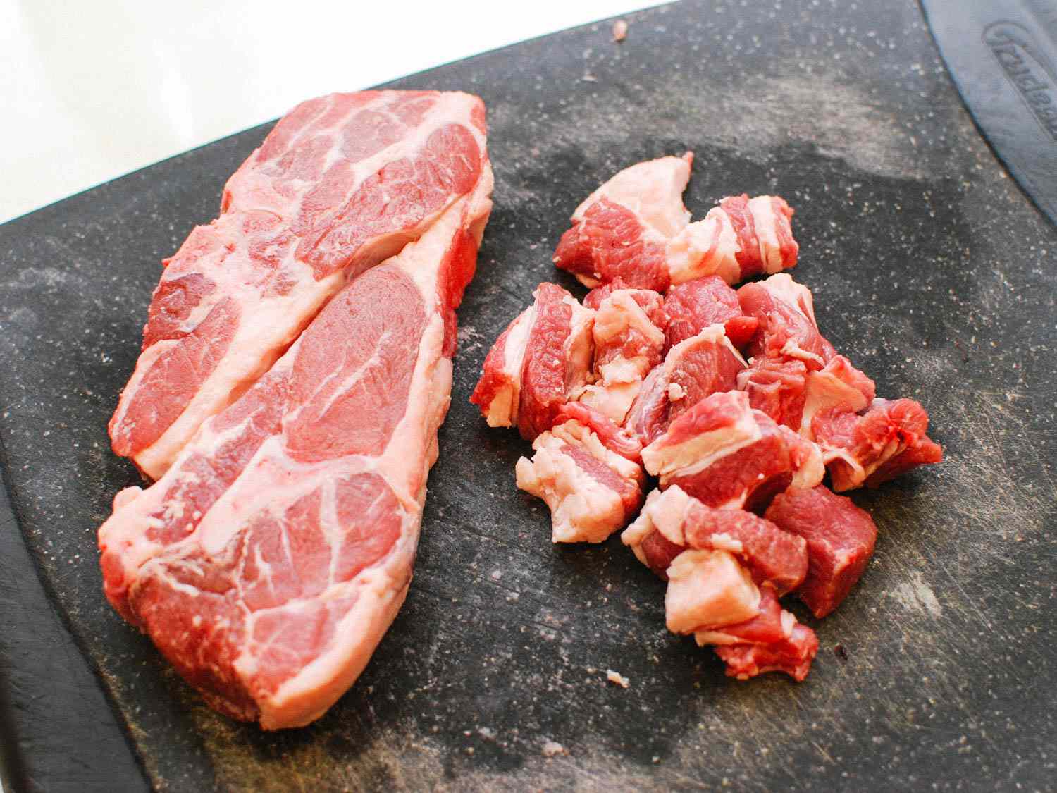 Two lamb shoulder chops resting on a cutting board alongside some cubed lamb shoulder.