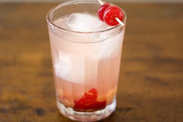 Closeup of a sour cherry gin cocktail, served in a glass with sour cherry garnish.