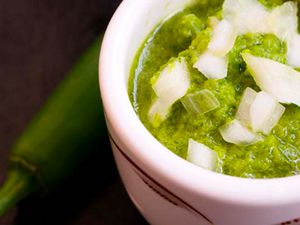 A ramekin of serrano salsa verde with diced white onion on top. 