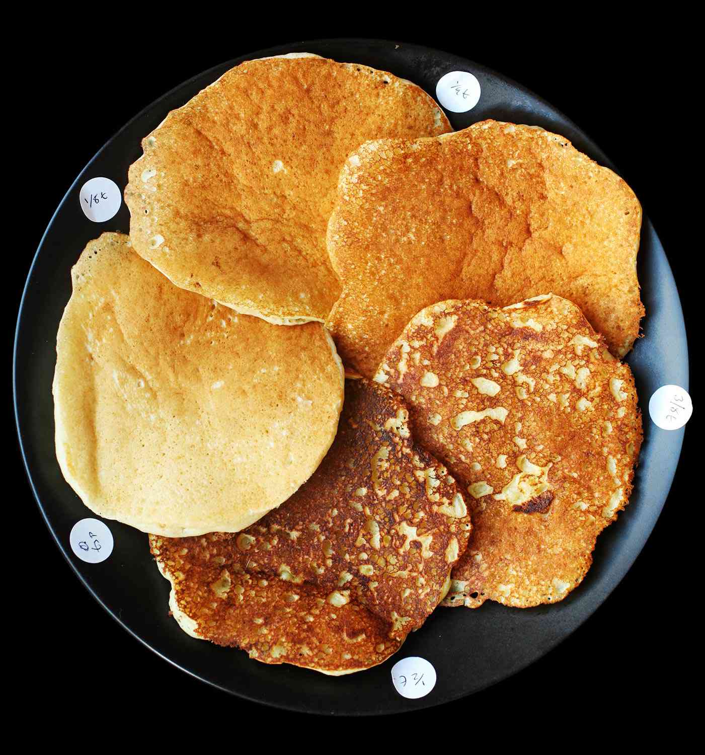 A black plate with five overlapping pancakes of varying shades of brown